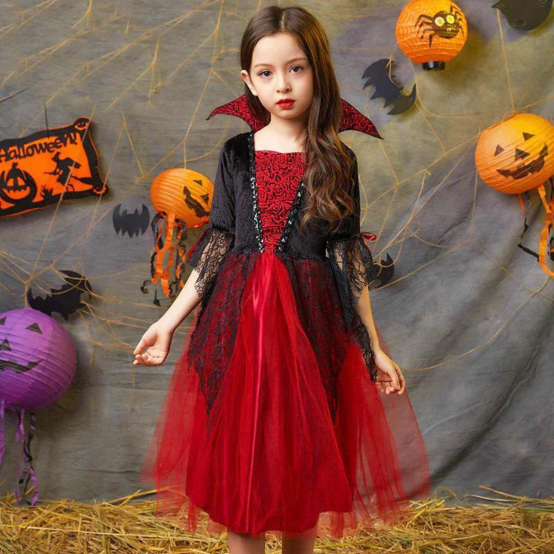 Young girl in red and black vampire Halloween dress with bat wings, surrounded by Halloween decor