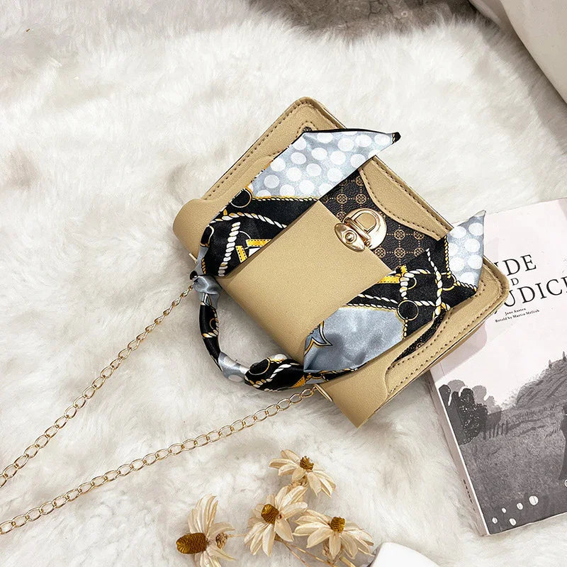 Beige handbag with gold clasp and chain strap, decorated with black and silver patterned scarf, on white fur surface