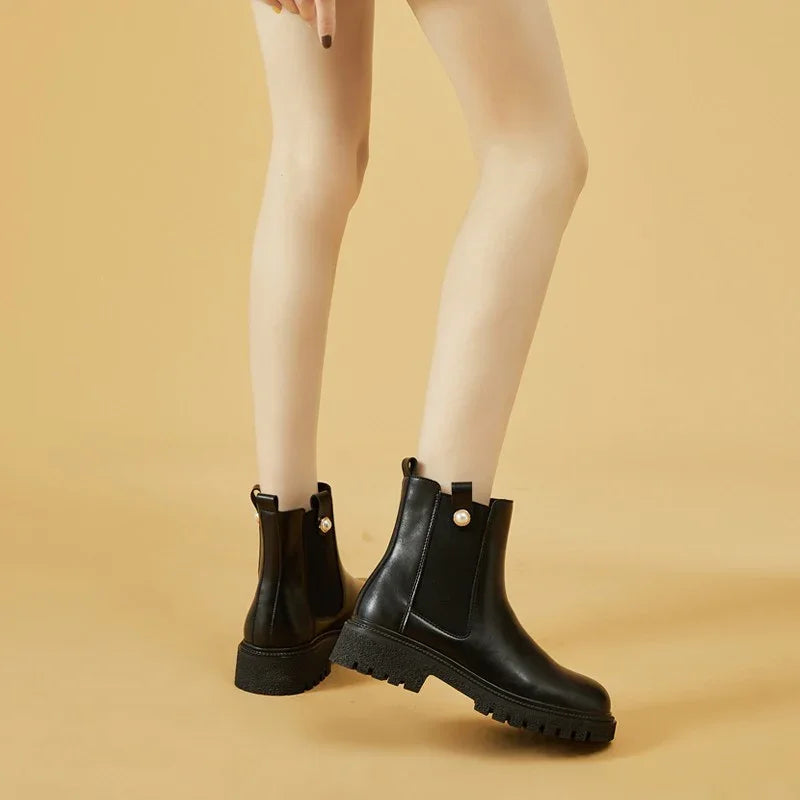 legs wearing black leather ankle boots with chunky sole and pearl detail on beige background