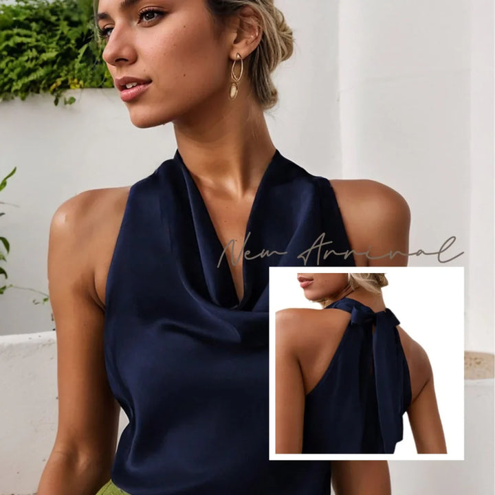 Woman wearing a navy blue satin halter top with cowl neckline and back tie detail