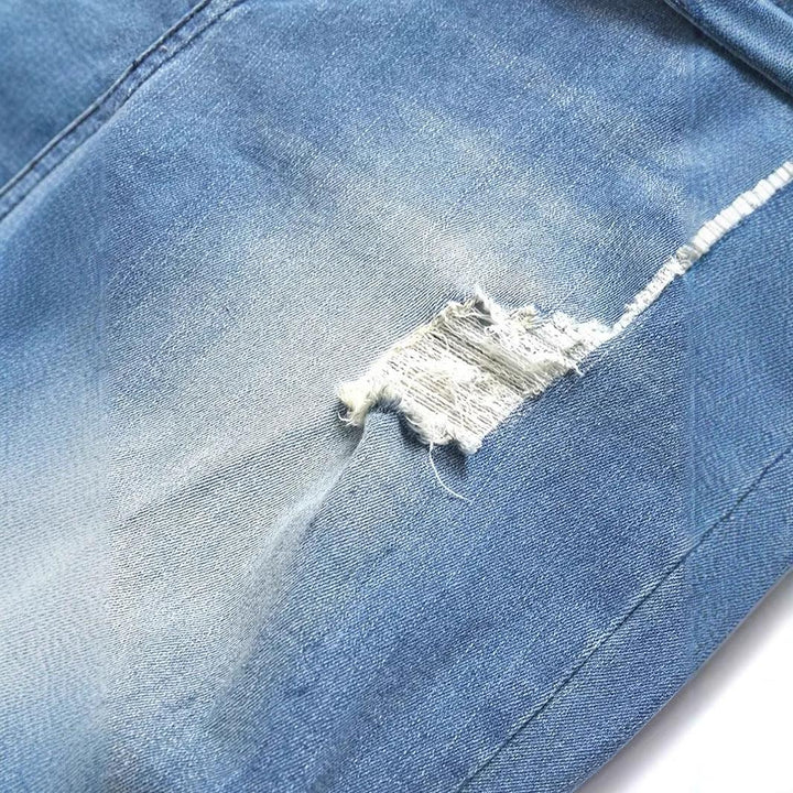 Close-up of light blue distressed denim jeans with a frayed tear detail