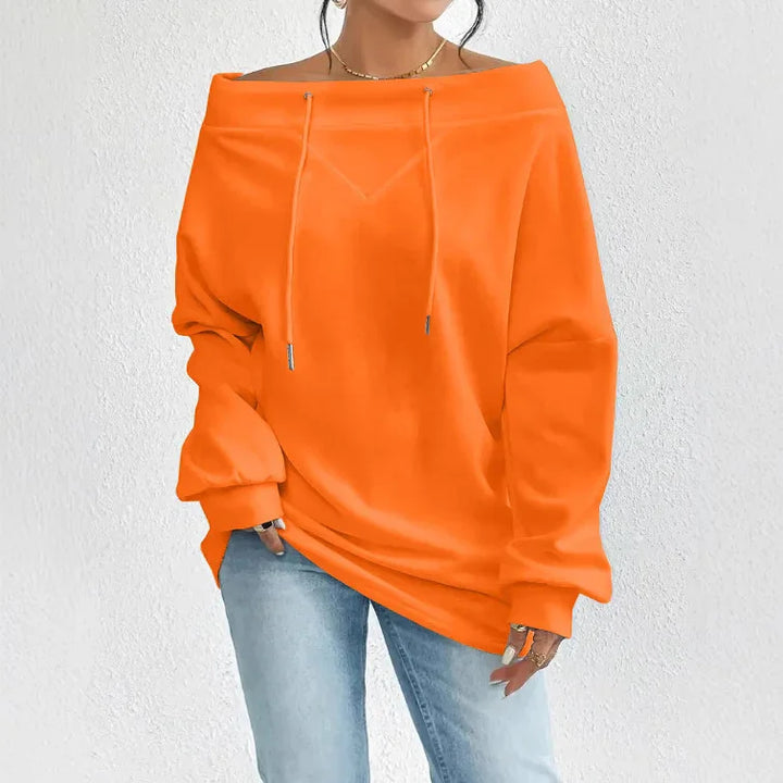 Woman wearing bright orange off-shoulder oversized sweatshirt with drawstrings and light blue jeans