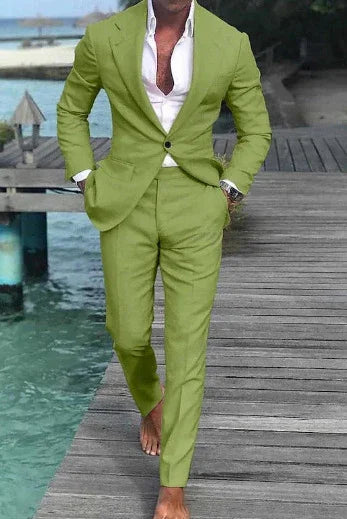 Man wearing a lime green suit with a white shirt, standing barefoot on a wooden dock by turquoise water