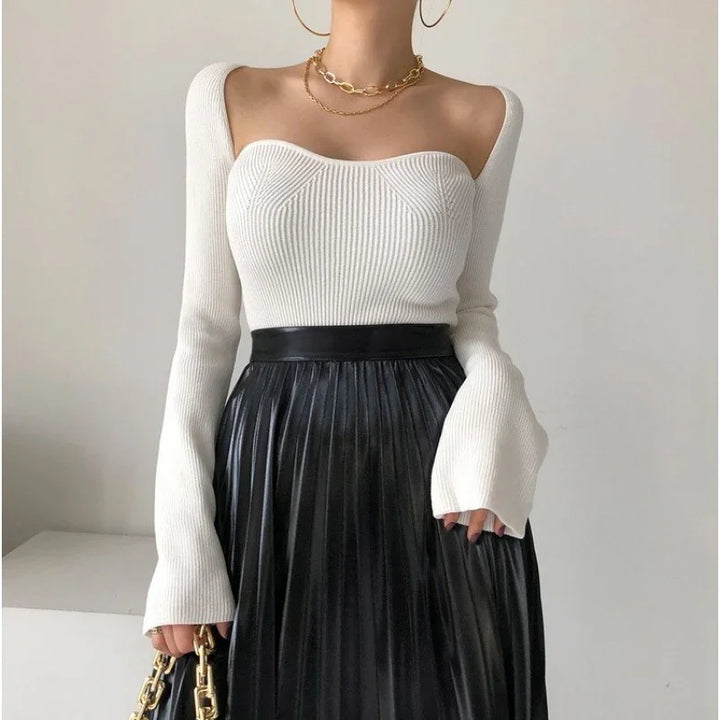 Woman wearing a white ribbed long-sleeve top with a sweetheart neckline and a black pleated leather skirt
