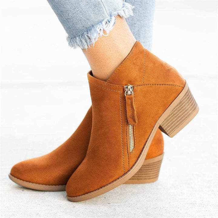 Woman wearing tan suede ankle boots with side zipper and stacked block heel, paired with frayed light blue jeans