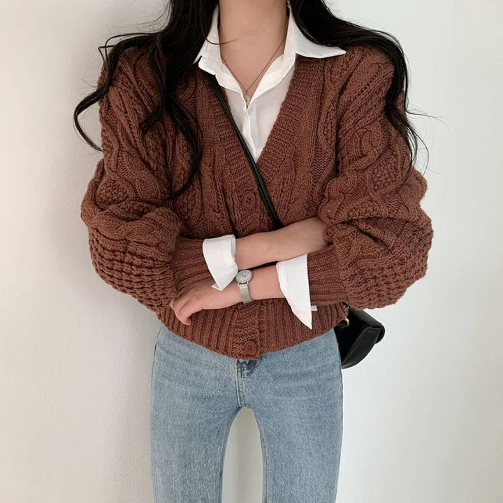 Woman wearing brown chunky cable knit cardigan over white shirt with light blue jeans and silver wristwatch