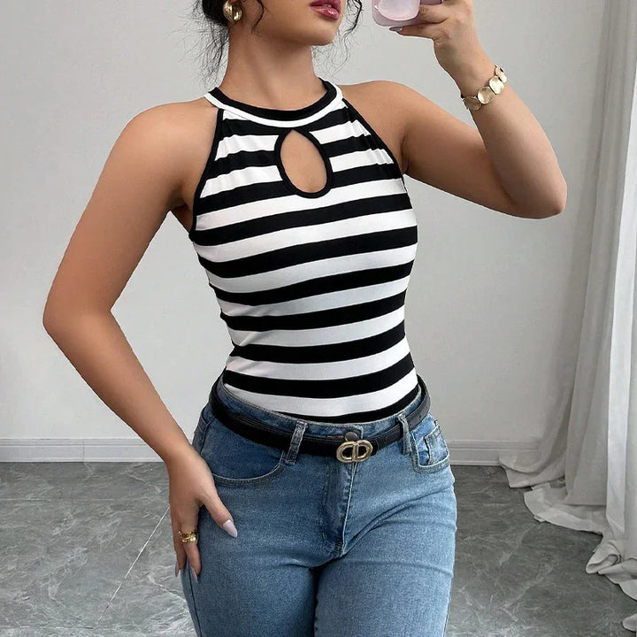Woman in black and white striped sleeveless top with keyhole neckline and blue jeans taking selfie indoors