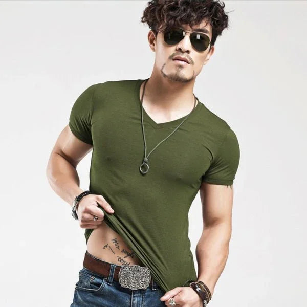 Young man wearing olive green fitted t-shirt, sunglasses, and jeans with tattoo visible on abdomen