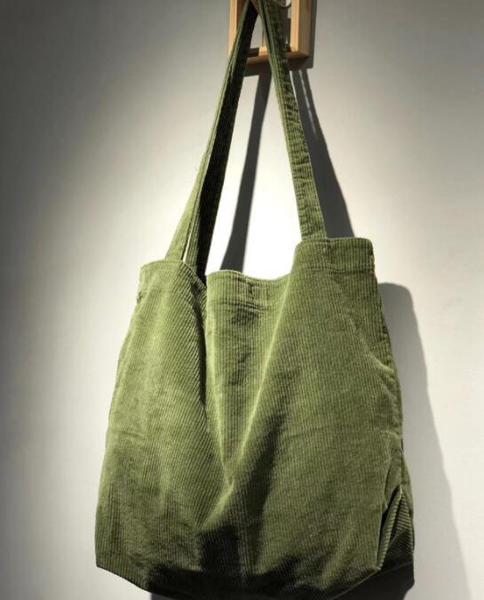 Green corduroy tote bag hanging on a wall with long straps and soft texture