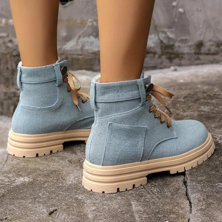 Light blue fabric ankle boots with beige rugged soles and brown laces on concrete surface