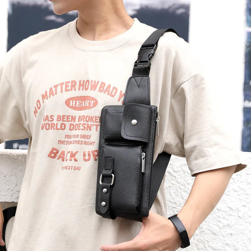 Person wearing beige graphic t-shirt and black leather crossbody sling bag with zip and buckle details