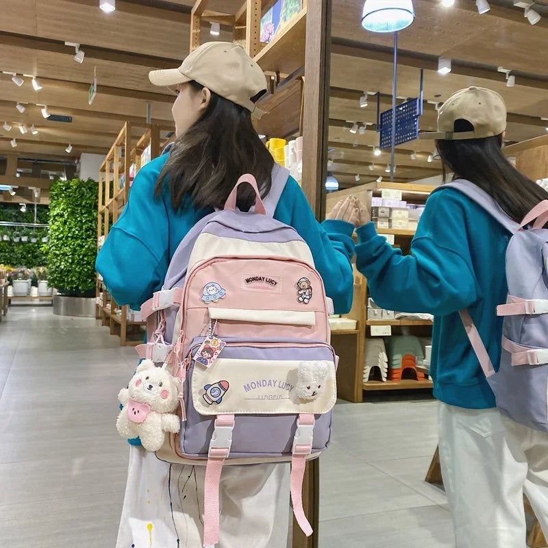 Woman in beige cap and teal sweatshirt wearing pastel pink and lavender Monday Lucy backpack with plush toy in modern store