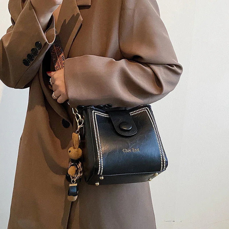 Woman wearing brown coat carrying black leather Chie 2nd handbag with decorative strap and keychain