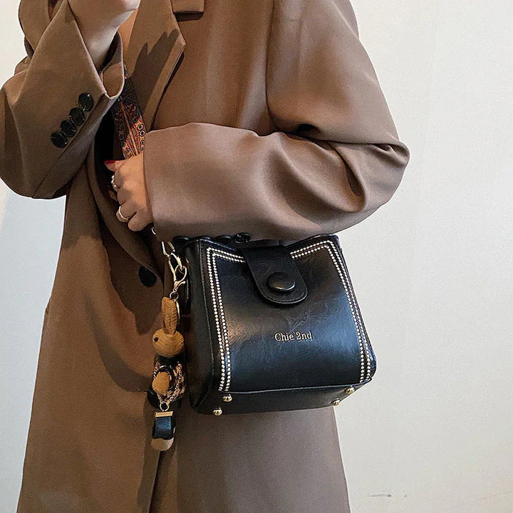 Woman wearing brown coat carrying black leather Chie 2nd handbag with decorative strap and keychain