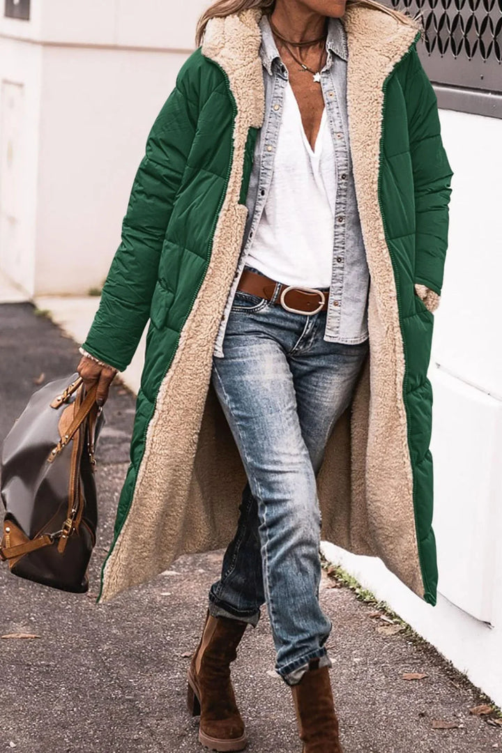 Woman wearing green sherpa-lined long coat, denim jeans, white shirt, brown boots, holding brown handbag