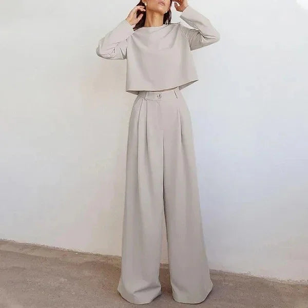 Woman wearing beige wide-leg trousers and matching long-sleeve cropped top against plain wall