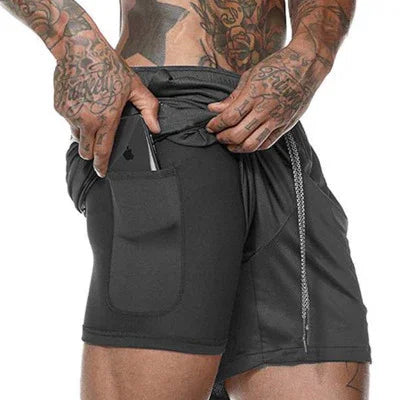 Tattooed man wearing black athletic shorts with side pocket holding a smartphone