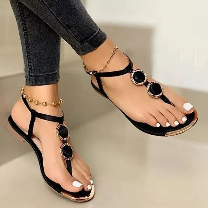 Black flat sandals with gold accents and decorative stones worn with black jeans and gold anklet
