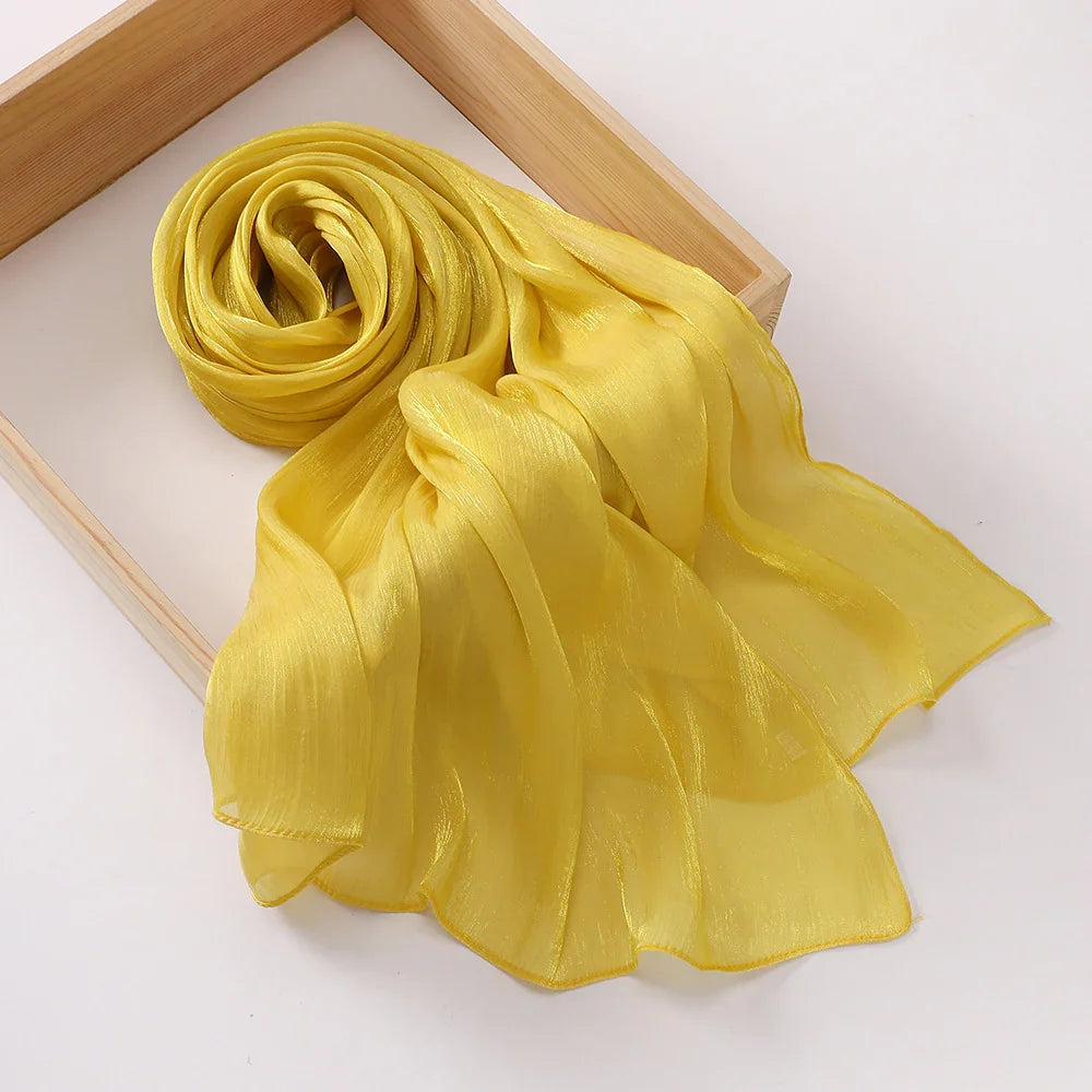 Yellow sheer silk scarf rolled and draped inside a light wooden box on white background
