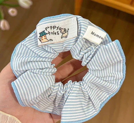 Blue and white striped fabric hair scrunchie with playful dog and house embroidery labeled Poppy Tails and tag reading Momow