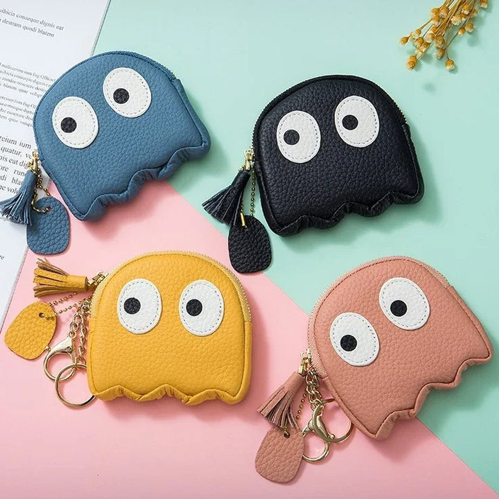Four colorful ghost-shaped leather coin purses with large eyes and tassel keychains on pastel background