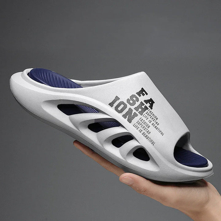 White and navy slip-on sandal with cutout sides and text design, held against gray background