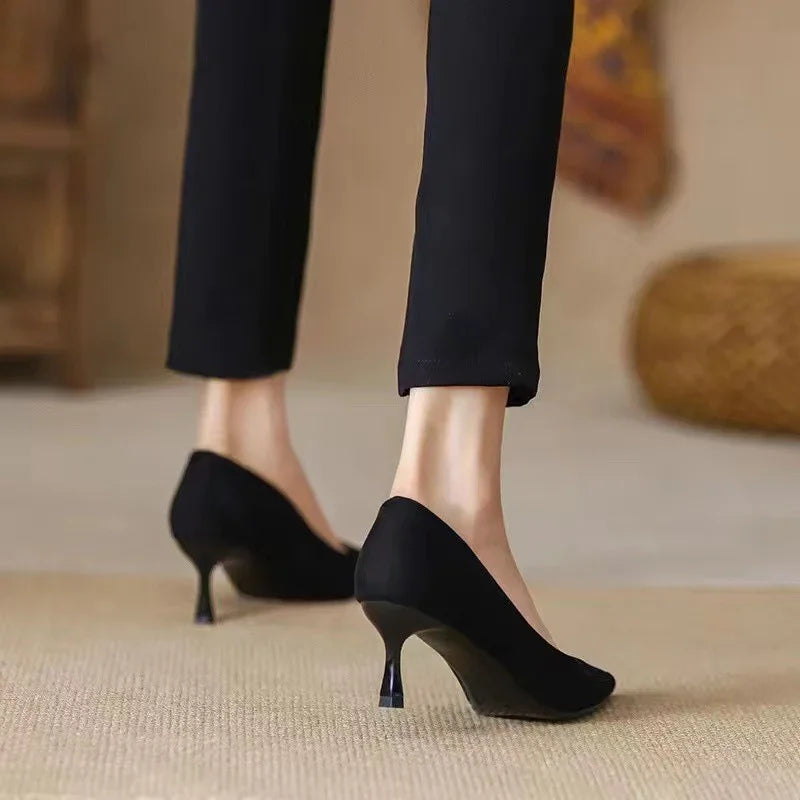 Woman wearing black kitten heel pumps with slim heels paired with black pants on beige carpet