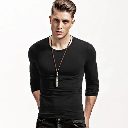 Young man wearing a fitted black long-sleeve shirt and pendant necklace against white background