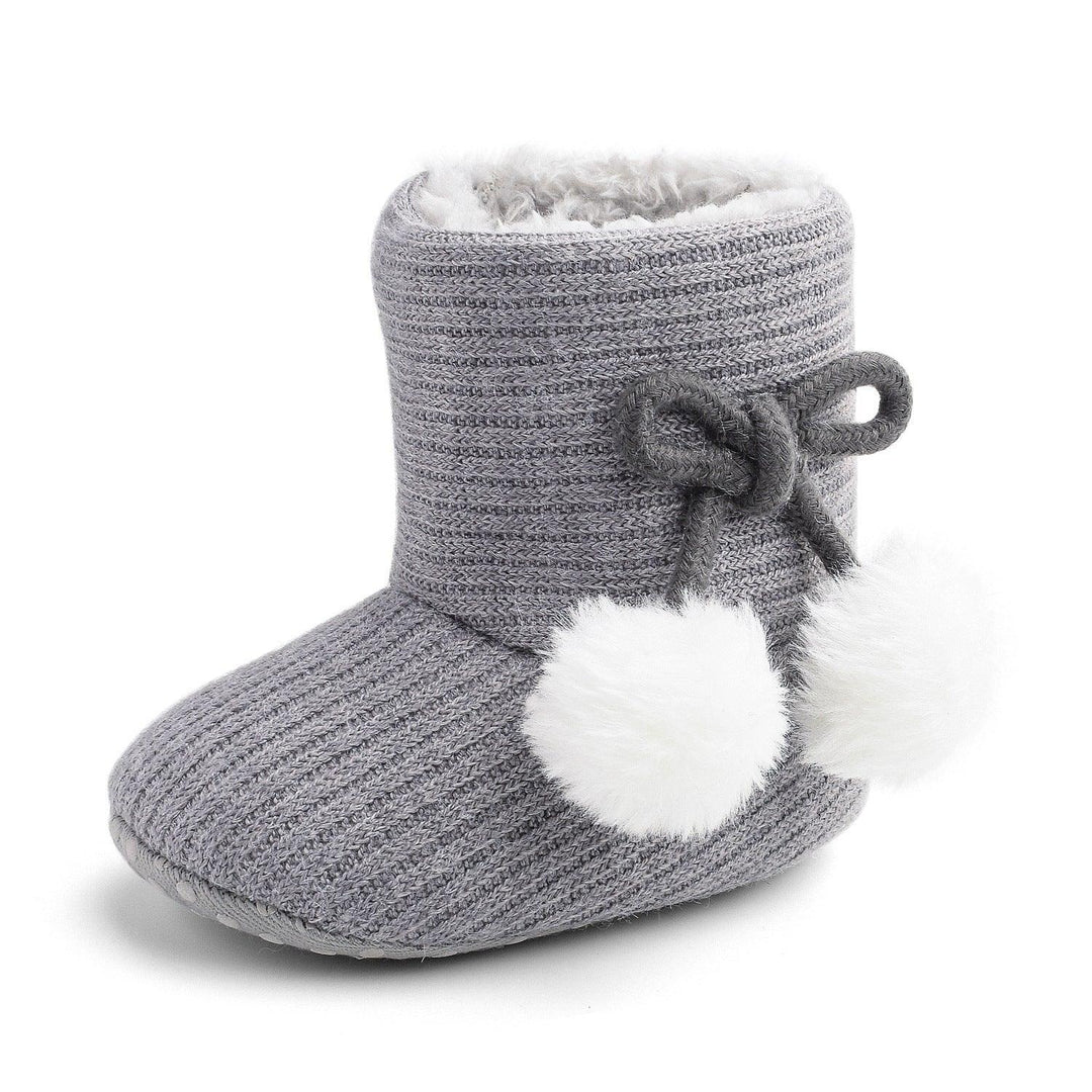 Gray knitted baby bootie with white fuzzy pom-poms and soft inner lining