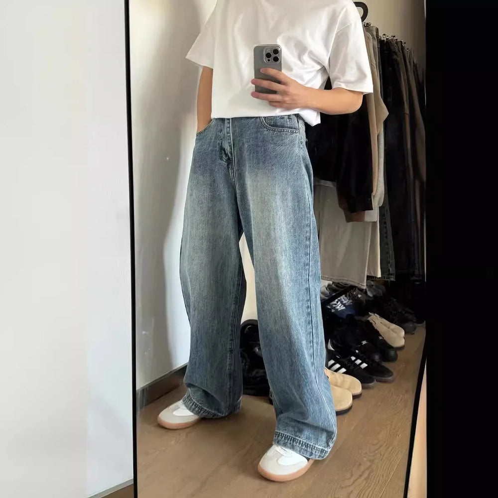 Person wearing loose light blue denim jeans, white t-shirt, and white sneakers, taking mirror selfie indoors
