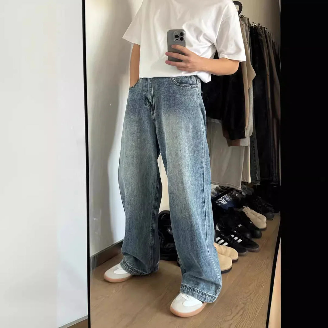 Person wearing loose light blue denim jeans, white t-shirt, and white sneakers, taking mirror selfie indoors