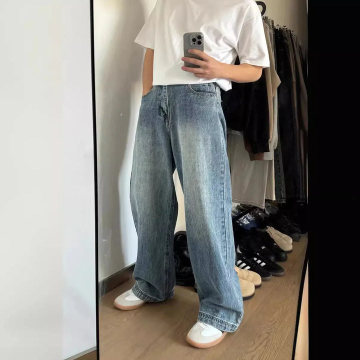 Person wearing loose light blue denim jeans, white t-shirt, and white sneakers, taking mirror selfie indoors