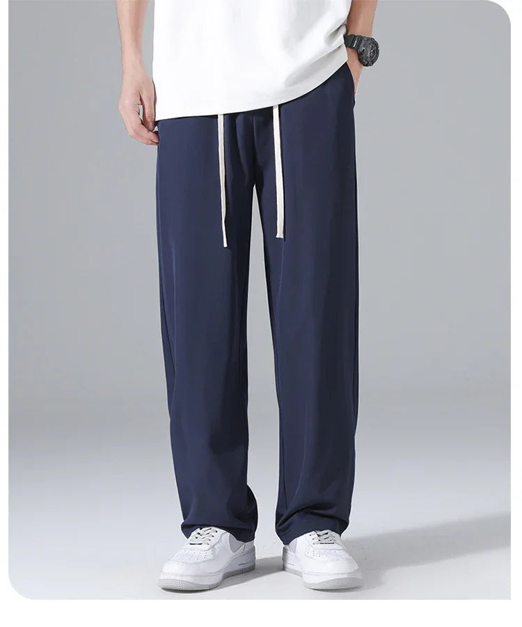 Man wearing navy blue casual pants with white drawstrings and white sneakers, standing against gray background