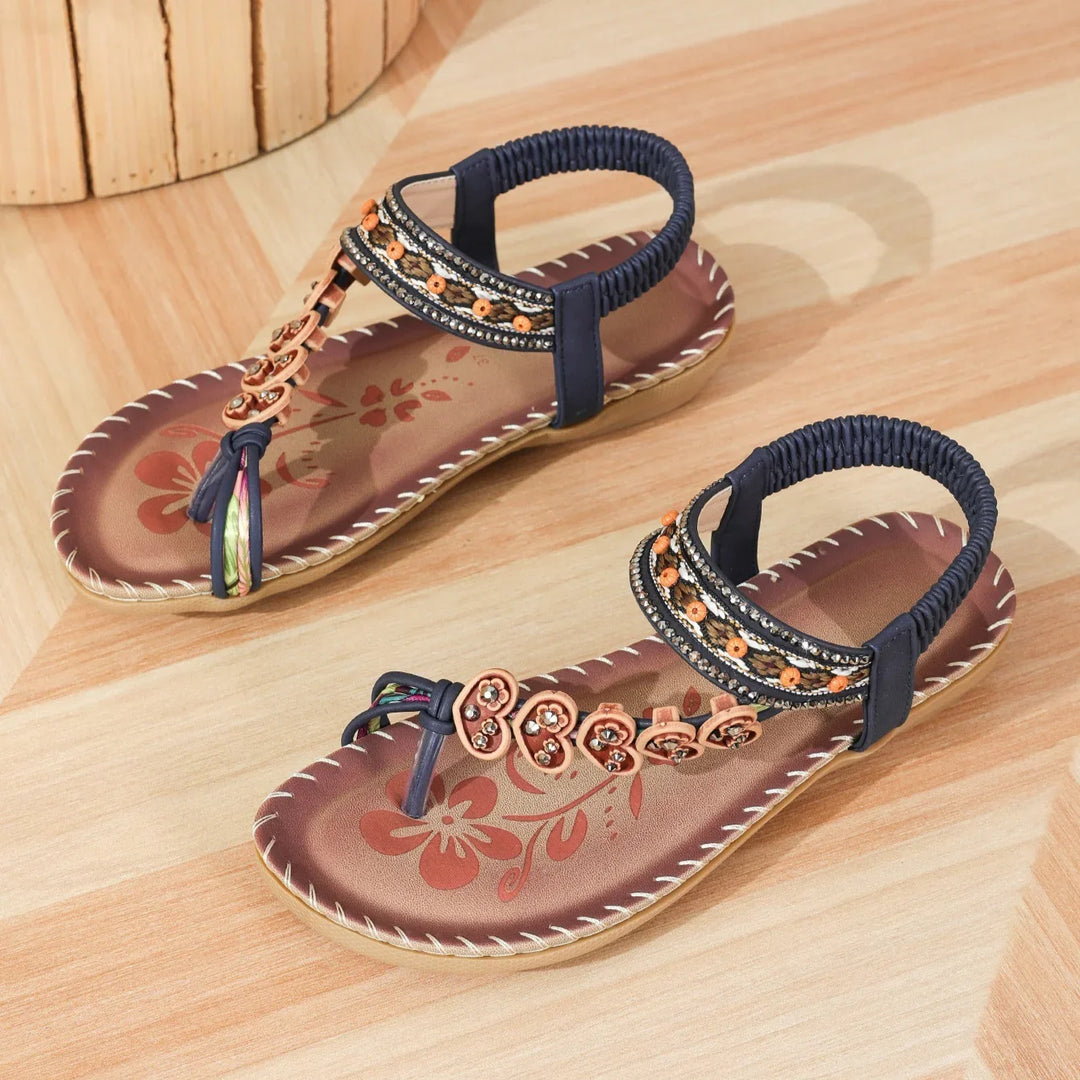 Women's brown floral thong sandals with navy straps and decorative orange beads on wooden floor