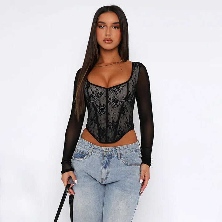 Woman wearing black lace corset top with long sheer sleeves and light blue jeans holding black purse