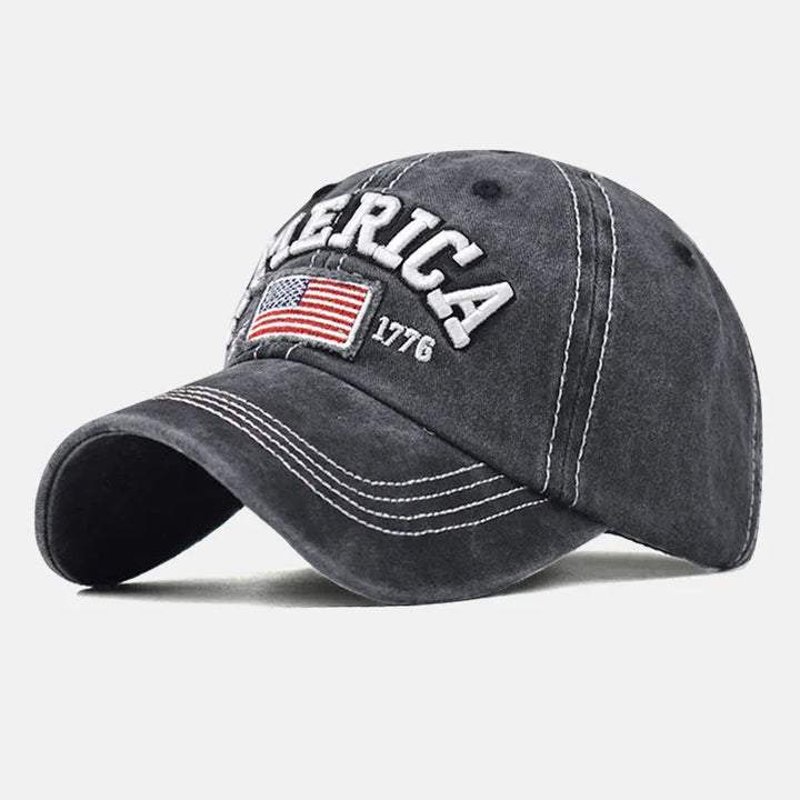 Dark gray baseball cap with white stitching, embroidered American flag, and text 'AMERICA 1776'