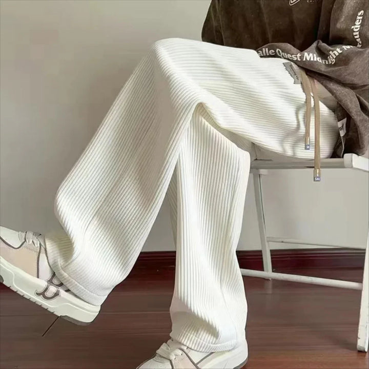 Person wearing white ribbed wide-leg pants and sneakers seated on a white chair indoors
