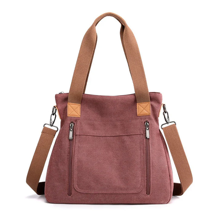Pink canvas tote bag with brown handles and detachable shoulder strap, front zipper pockets