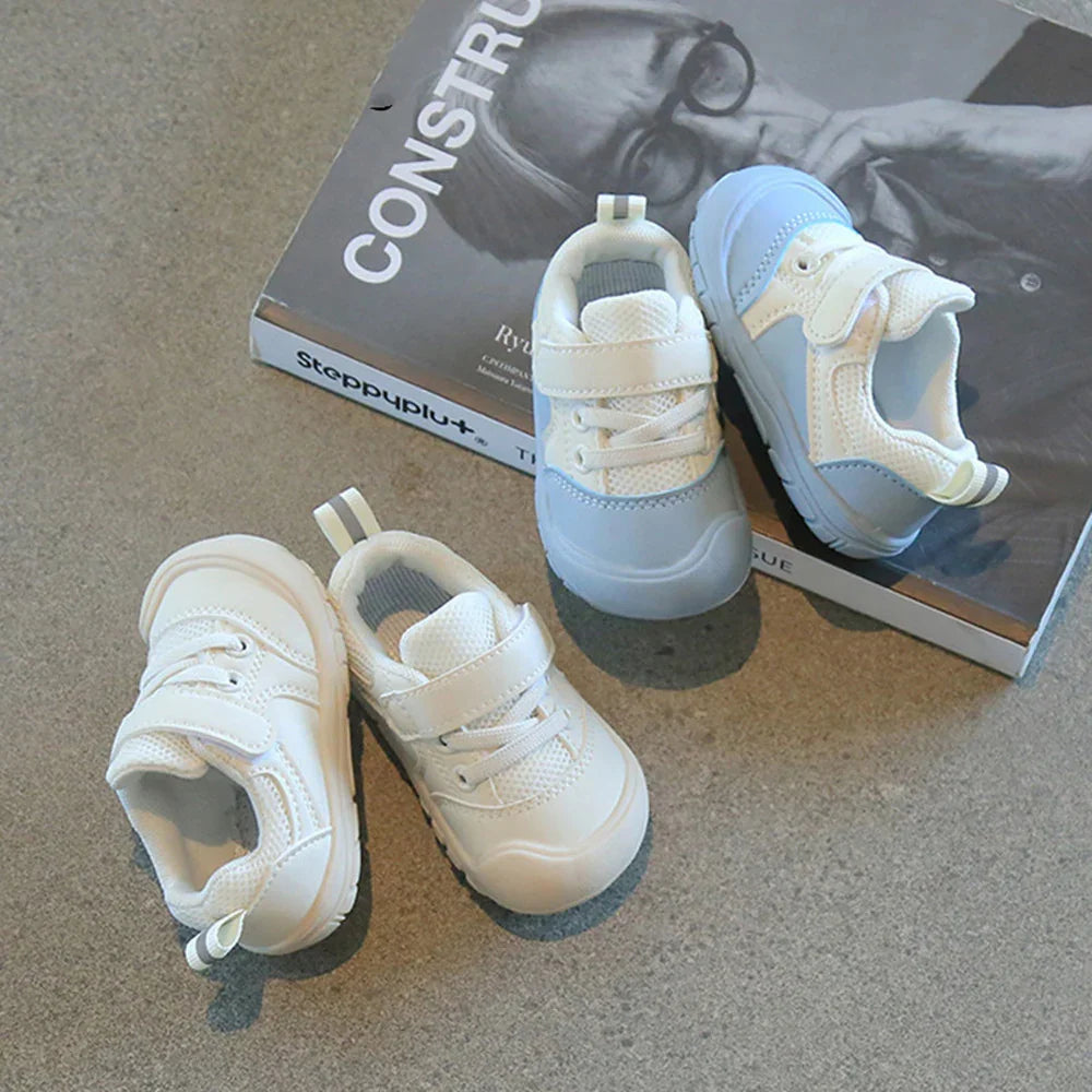 Pair of white and light blue toddler sneakers with velcro straps on a gray surface near a magazine