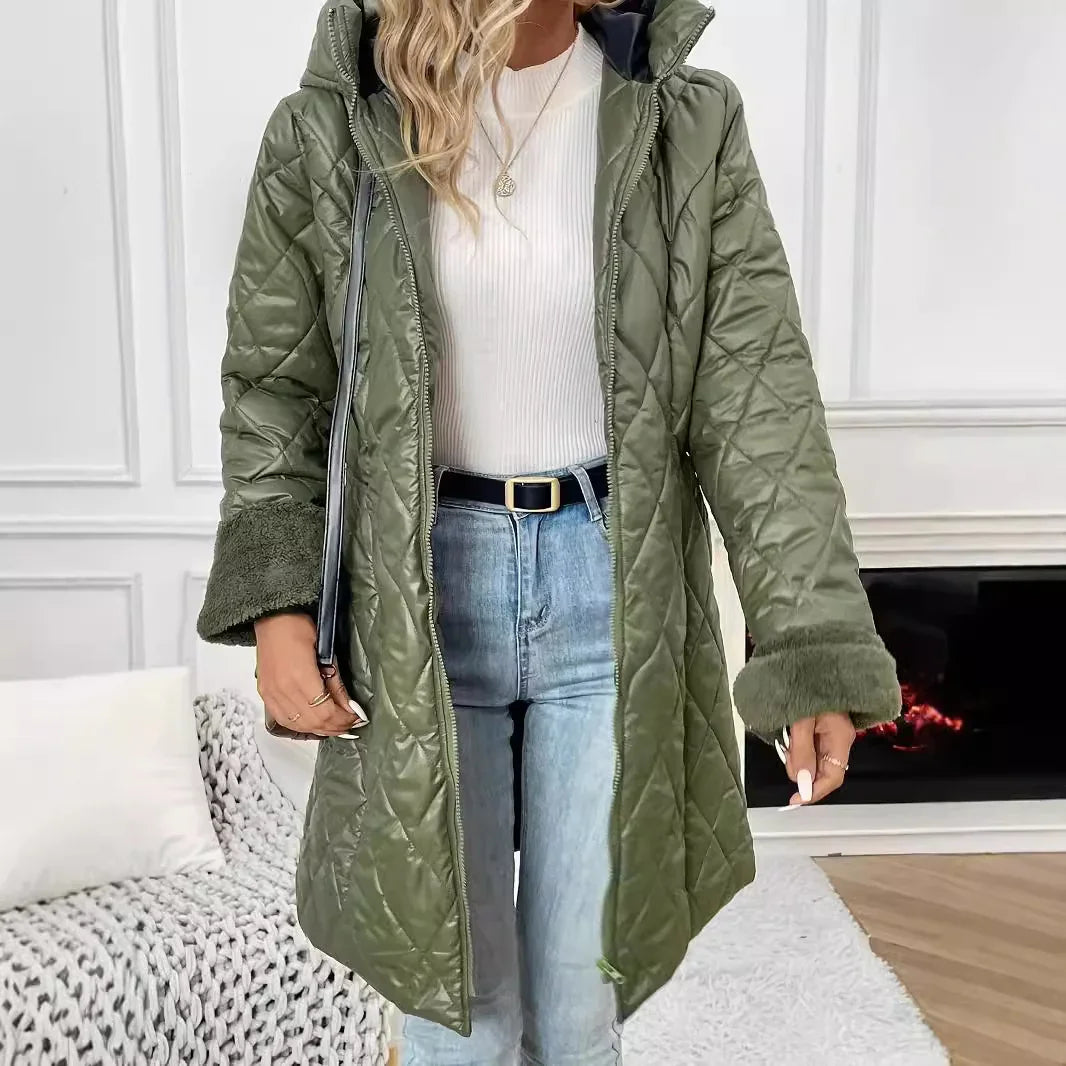 Woman wearing olive green quilted winter coat with faux fur cuffs over white ribbed top and light blue jeans