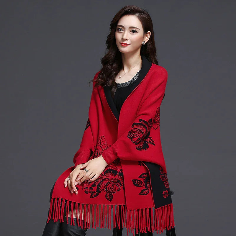 Woman wearing red floral knit shawl with fringe details, seated against dark background