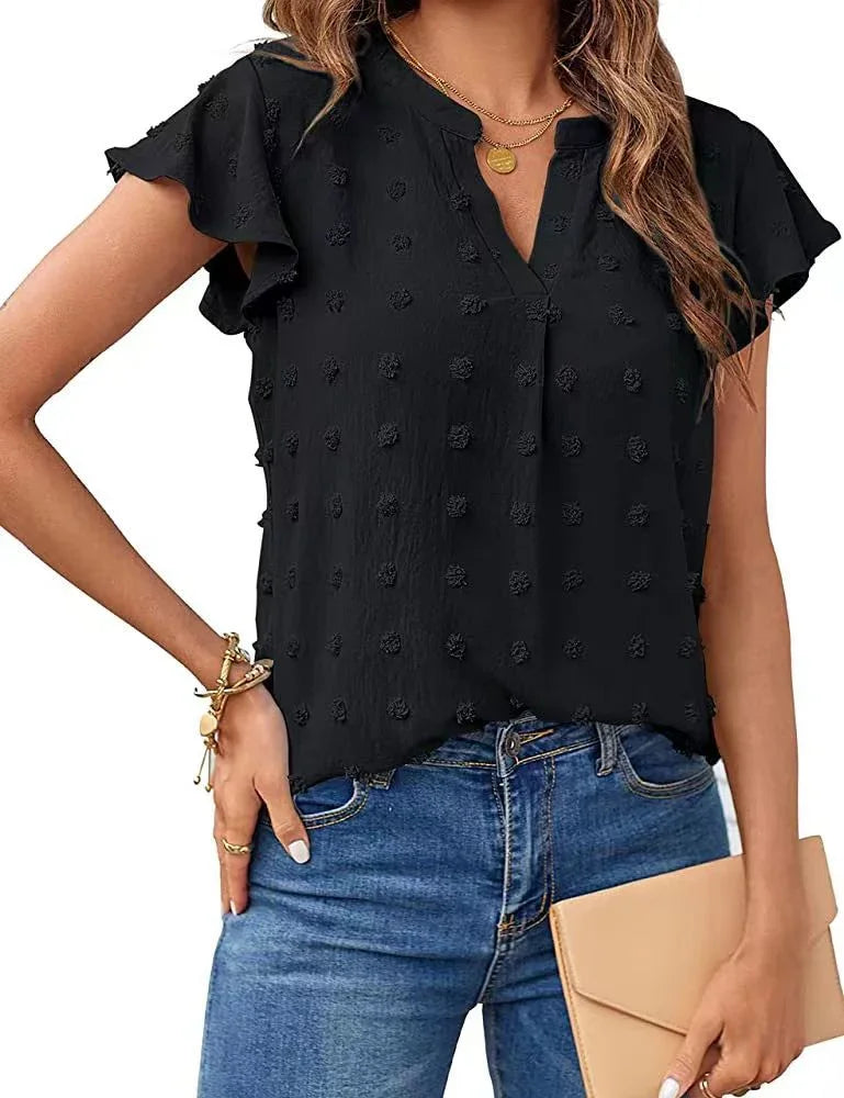 Woman wearing black textured short sleeve blouse with ruffle sleeves and blue jeans holding tan clutch