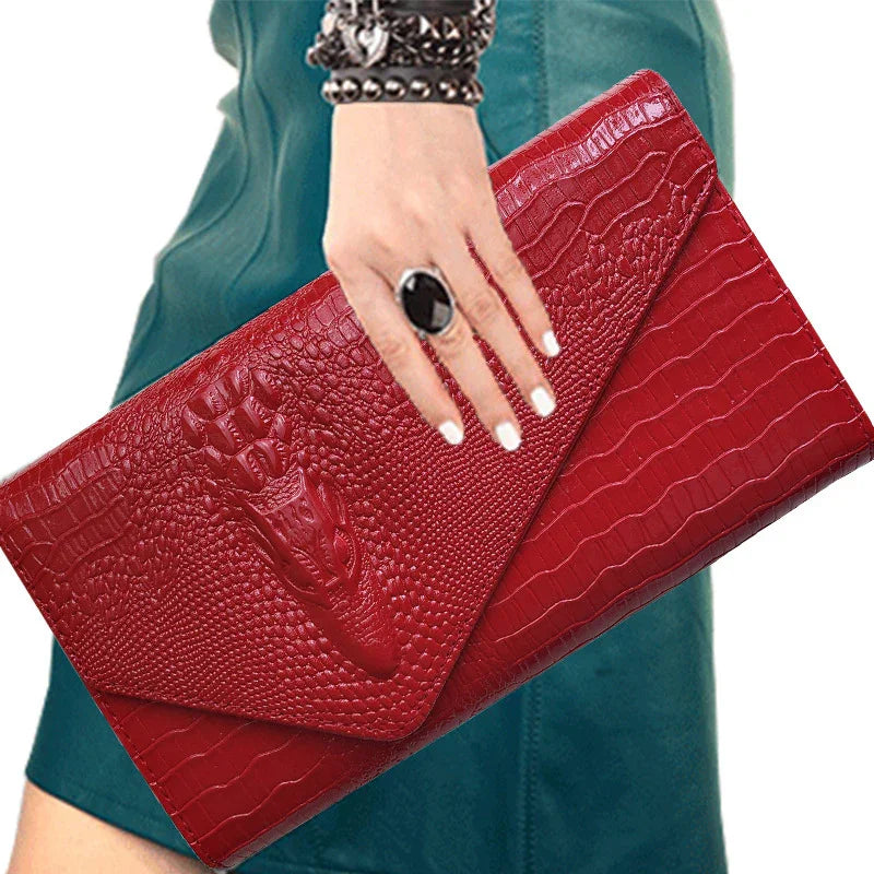 Woman holding red crocodile embossed leather clutch bag with black ring and studded bracelet