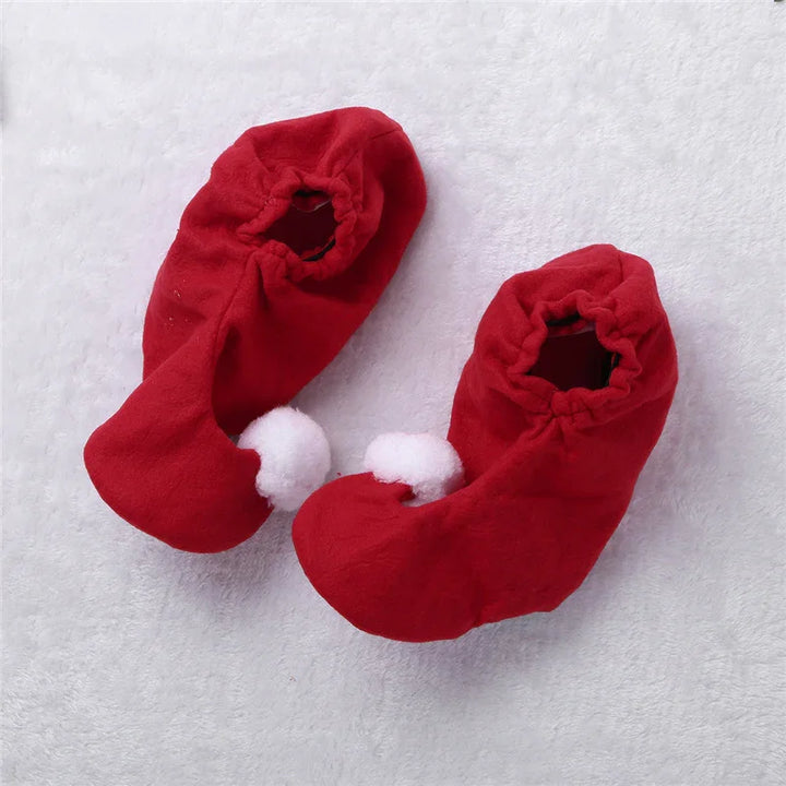 Red soft toddler slippers with white pom-poms on a white textured background