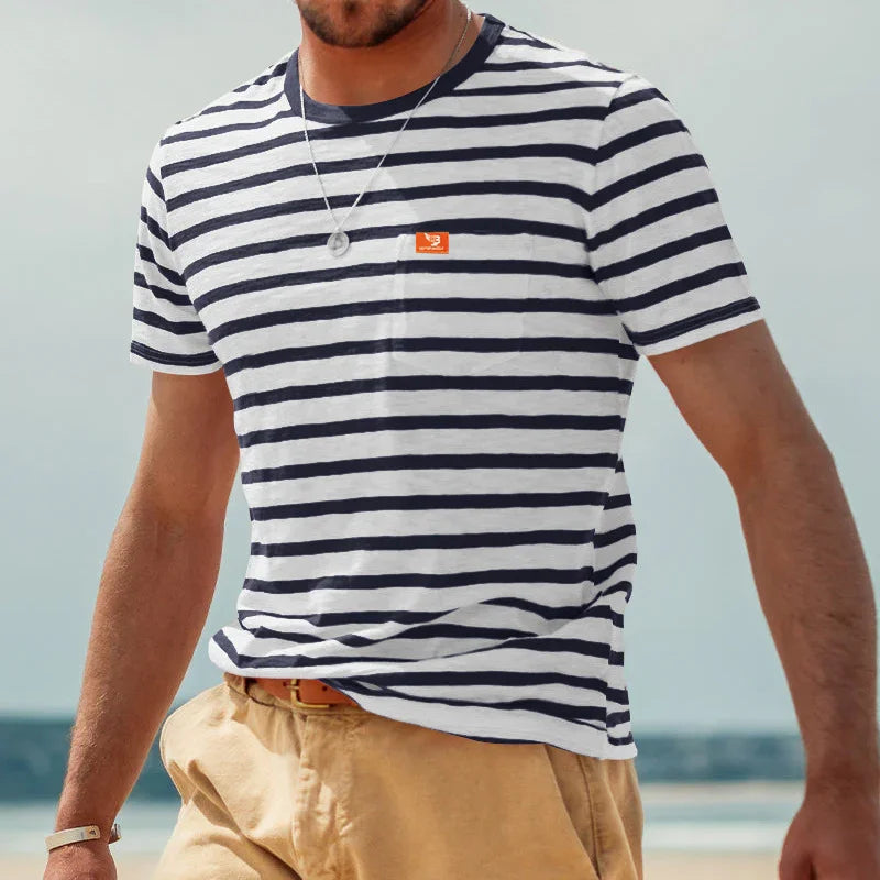 Man wearing navy and white striped t-shirt with orange logo and beige pants by the beach