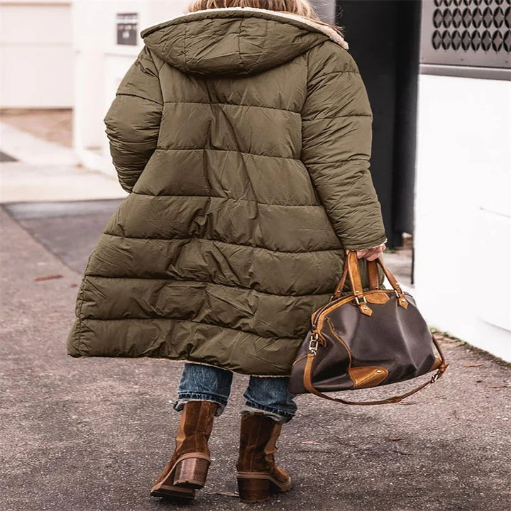 Person wearing long olive green puffer coat with hood, cuffed jeans, and brown heeled boots, carrying brown leather handbag outdoors