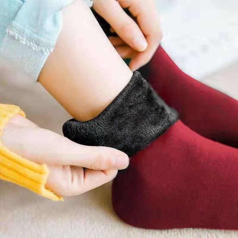 Close-up of hands adjusting black fleece-lined warm socks on a foot wearing maroon socks with yellow sleeve visible