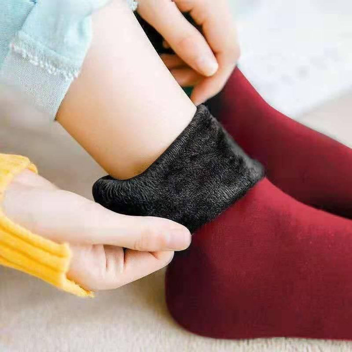 Close-up of hands adjusting black fleece-lined warm socks on a foot wearing maroon socks with yellow sleeve visible