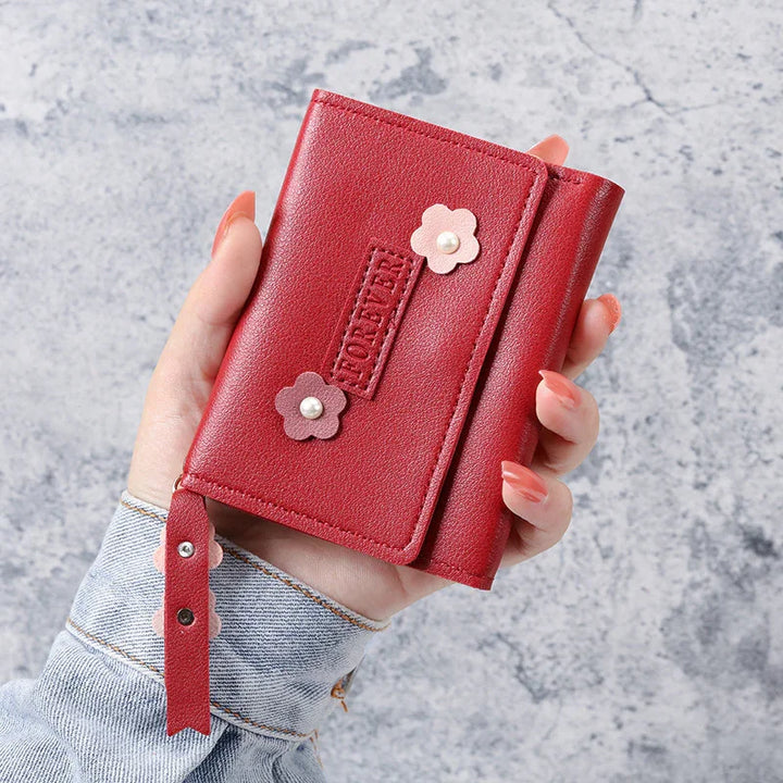 Hand holding red leather wallet with floral pearl accents and wrist strap on gray background