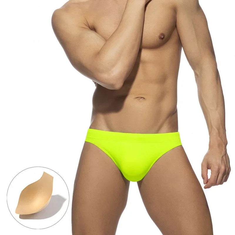Fit male model wearing neon yellow men's swim briefs with removable beige padding insert
